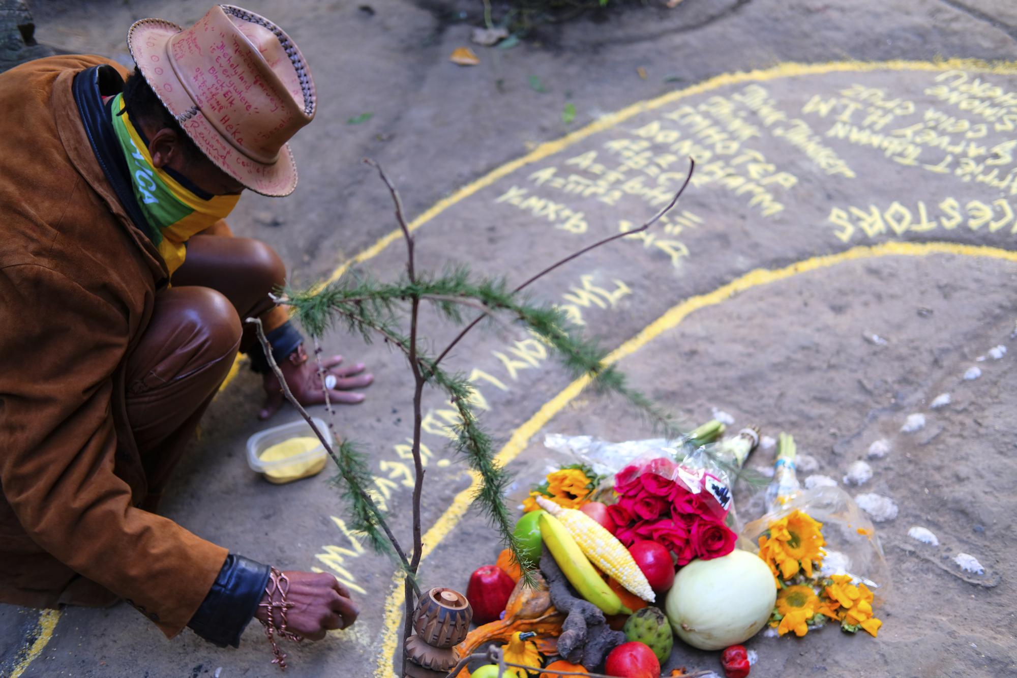 Paul Gentles, a Jamaican artist and member of the Rastafari faith, uses cornmeal to decorate an offering of fruits and flowers during a drumming circle at Brooklyn’s Prospect Park on Sunday, Oct. 24, 2021. As public opinion and policy continues to shift across the world toward the medicinal and recreational use of cannabis, some Rastafari adherents are questioning their place in the  legal market of the herb that they consider sacred. (AP Photo/Luis Andres Henao)