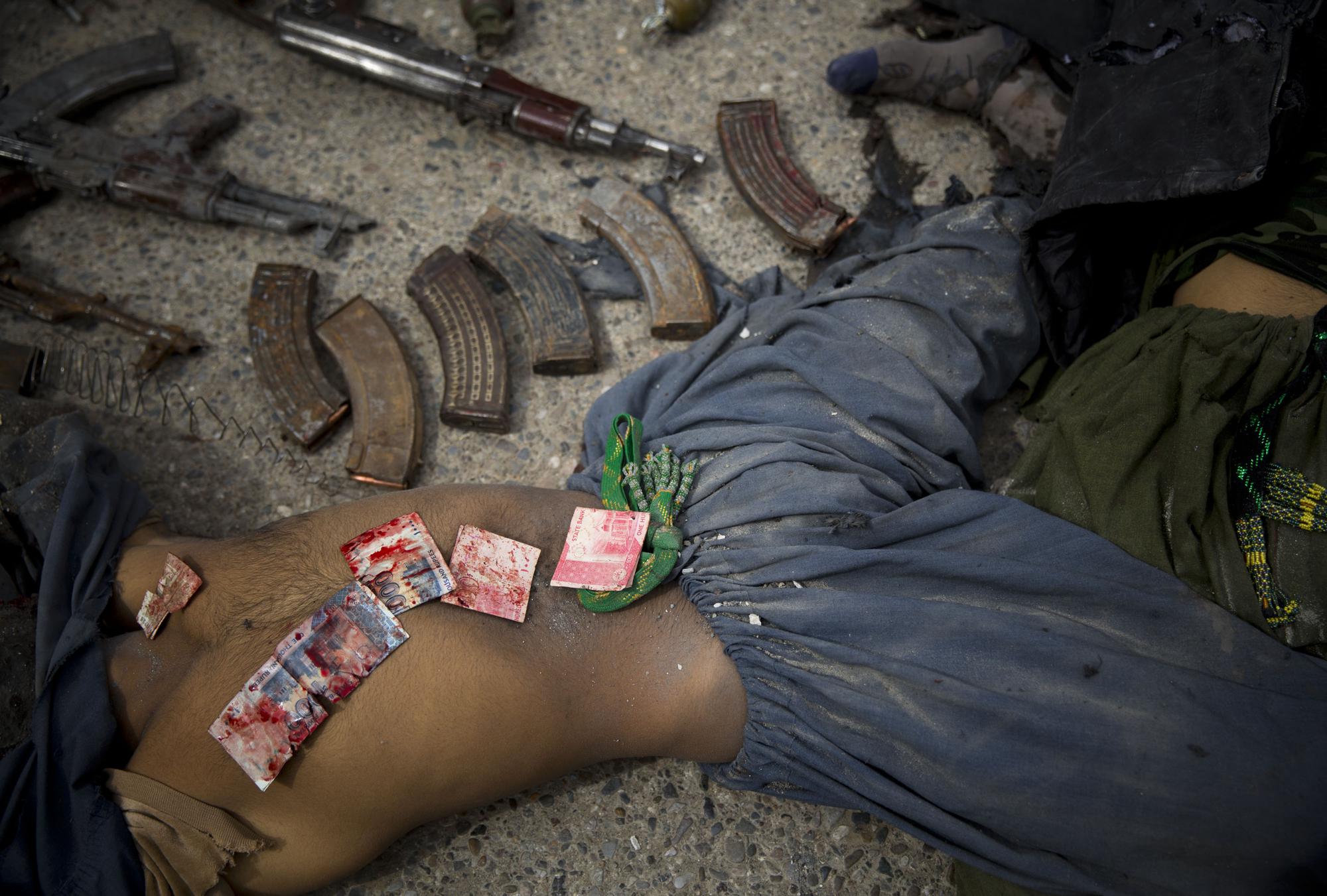 Pakistani bank notes covered in blood are displayed on the body of a dead suicide bomber after police found them in his pocket in the center of Kandahar, Afghanistan, Wednesday, March 12, 2014, after an attack on the former Afghan intelligence headquarters. Police officials said three insurgents who tried to storm the former headquarters of Afghanistan's intelligence service in southern Kandahar died in a gunbattle with security forces. (AP Photo/Anja Niedringhaus)