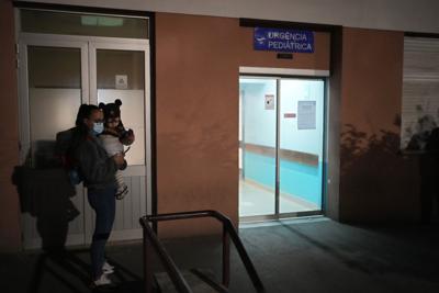 Una mujer con una niña esperan en el ingreso a la sala de emergencias del Hospital Garcia de Orta en Almada, al sur de Lisboa, el 30 de noviembre del 2021. El hospital dijo que cerraba su sala de pediatría luego de trascender que un empleado que había estado en contacto con miembros de un club de fútbol en el que hay un brote de ómicron había contraído esa variante del coronavirus. (AP Photo/Armando Franca)