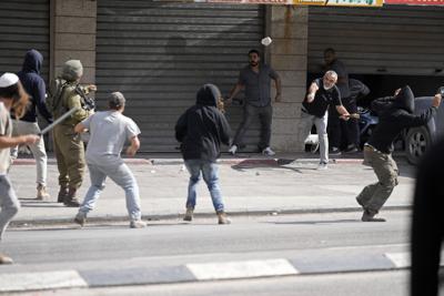 Un palestino lanza una piedra contra colonos israelíes y un soldado israelí durante enfrentamientos en Huwara, cerca de la localidad de Nablus, en Cisjordania, el jueves 13 de octubre de 2022. (AP Foto/Majdi Mohammed)