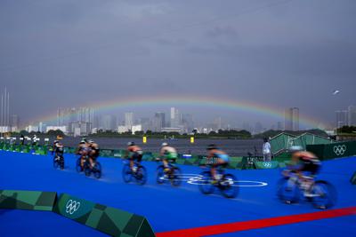 Con un arco iris de fondo, las mujeres del triatlón disputan la prueba ciclística en los Juegos Olímpicos de Tokio el 27 de julio del 2021. Algunos dicen que esta edición olímpica son los "Juegos del Arco Iris" por la creciente presencia, y aceptación, de los deportistas LGBTQ. (AP Photo/David Goldman)