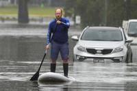 A man paddles on a stand-up paddle board through a flooded street at Windsor on the outskirts of Sydney, Australia, Tuesday, July 5, 2022. Hundreds of homes have been inundated in and around Australia's largest city in a flood emergency that was impacting 50,000 people, officials said Tuesday. (AP Photo/Mark Baker)
