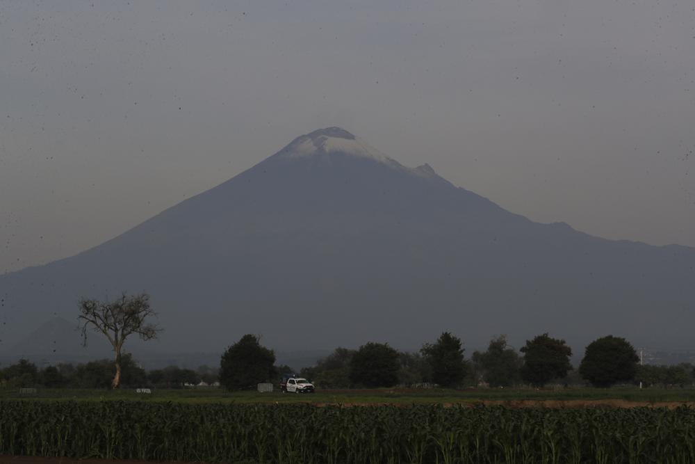 With the Popocatepetl volcano on the background, security personnel patrol the perimiter around a water filled sinkhole in Zacatapec, on the outskirts of Puebla, Mexico, Wednesday, June 9, 2021. The massive water-filled sinkhole continues swallowing farmers' fields in the central Mexican state of Puebla. (AP Photo/Fernando Llano)