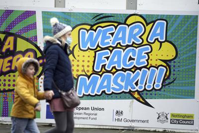 Unas personas caminan frente a un letrero que invita a los ciudadanos a portar una mascarilla para frenar la propagación del COVID-19 en Nottingham, Inglaterra, el lunes 20 de diciembre de 2021. (Mike Egerton/PA vía AP)
