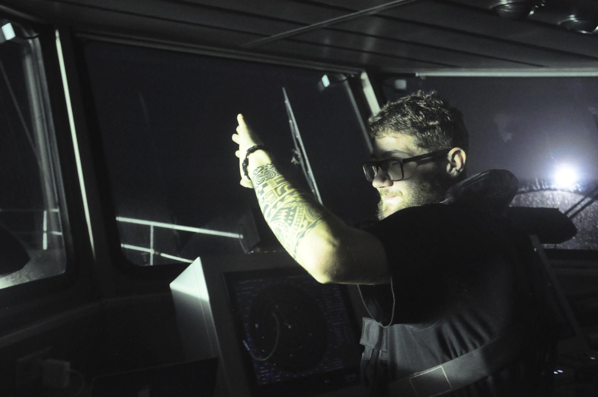 Filippo Marini, the third officer aboard the Ocean Warrior, shields his eyes from the light of several Chinese-flagged vessels fishing for squid at night on the high seas off the west coast of South America on July 19, 2021. Marini is an activist for Sea Shepherd, a Netherlands-based oceans conservation group. (AP Photo/Joshua Goodman)