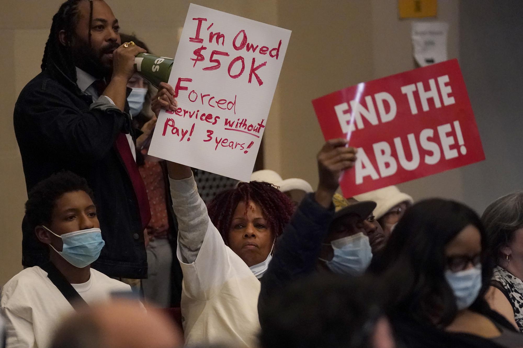 Seneca Scott, top left, yells as Pamela Haile, middle, holds up a sign with others during a Oakland City Council special community and economic development committee at City Hall in Oakland, Calif., Tuesday, April 11, 2023. Some landlords have gone without rental income for more than three years after Oakland, California approved an eviction moratorium in March 2020. (AP Photo/Jeff Chiu)
