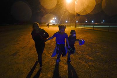 En esta imagen del 11 de mayo de 2021, tres migrantes se toman de las manos mientras corren bajo la lluvia en una zona de detención después de entregarse a las autoridades luego de cruzar la frontera desde México hacia Estados Unidos en Roma, Texas. (AP Foto/Gregory Bull, Archivo)