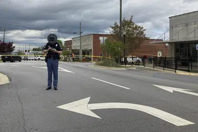 Un policía de Alabama revisa su teléfono mientras los investigadores trabajan en el lugar de un tiroteo fatal en el centro de Dadeville, Alabama, el domingo 16 de abril de 2023. (Foto AP/Jeff Amy)