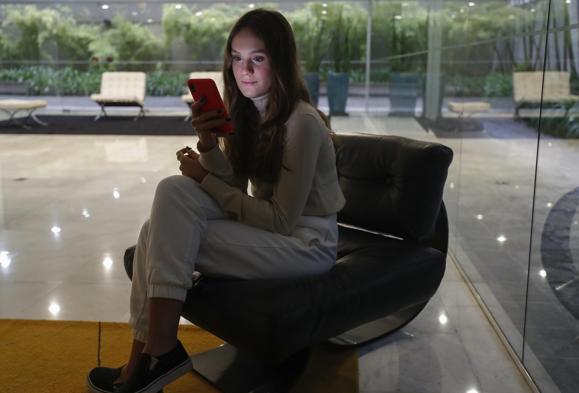 Manuela Salomao, 16, looks at her phone as she poses for a portrait in the lobby of her residential building in Sao Paulo, Brazil, Thursday, June 10, 2021. In Brazil, where COVID cases are still surging, she expressed frustration with her country's president, Jair Bolsonaro, whose government repeatedly ignored opportunities to buy vaccines. “The pandemic was not easy for a lot of people in Brazil. Many lost their jobs and could not socially distance because they needed to survive." (AP Photo/Andre Penner)