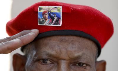 Un hombre con la emblemática boina roja del difunto presidente de Venezuela Hugo Chávez, adornada con una foto del actual presidente Nicolás Maduro con Chávez, saluda mientras espera para visitar los restos del líder en el sexto aniversario de su muerte, en esta fotografía de archivo del 5 de marzo de 2019, en Caracas. (AP Foto/Eduardo Verdugo)