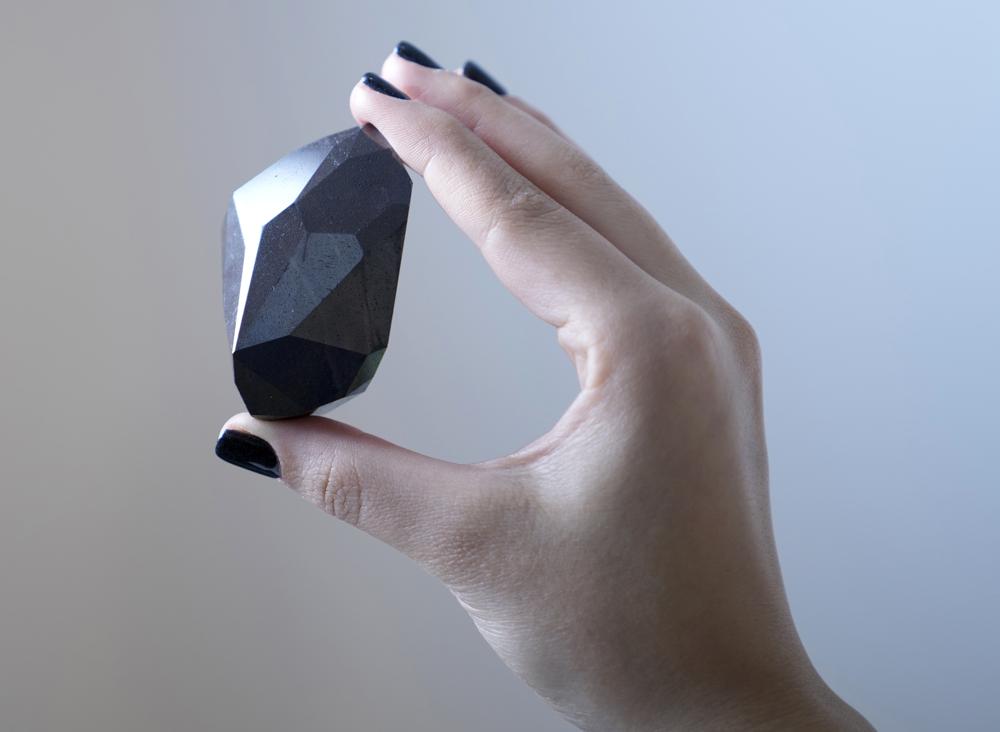 An employee of Sotheby's Dubai presents a 555.55 Carat Black Diamond "The Enigma" to be auctioned at Sotheby's Dubai gallery, in Dubai, United Arab Emirates, Monday, Jan. 17, 2022. (AP Photo/Kamran Jebreili)