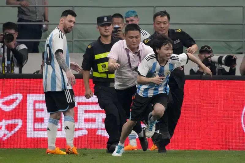 El delantero argentino Lionel Messi (izquierda) observa cuando la seguridad persigue a un aficionado durante un partido amistoso, el jueves 15 de junio de 2023, en Beijing. (AP Foto/Mark Schiefelbein)