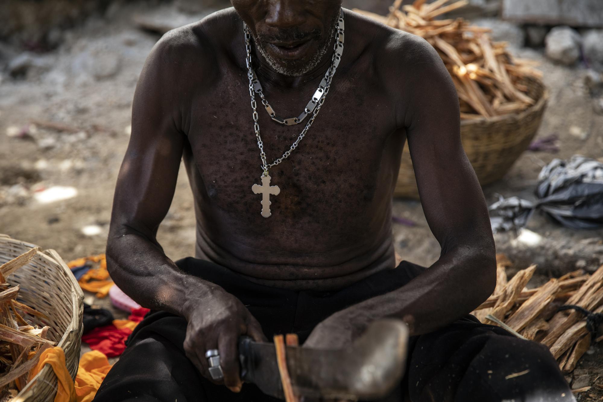 A vendor prepares kindling outside his home in the La Piste neighborhood of Port-au-Prince, Haiti, Friday, Sept. 17, 2021. The wealthy of Port-au-Prince live in the hillside eastern suburb of Petion-Ville in gated and privately guarded homes, largely protected from the violence and cost of payoffs. But the poor suffer rising prices and bottlenecks. (AP Photo/Rodrigo Abd)