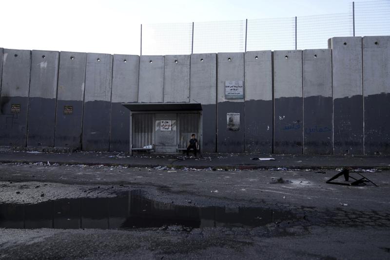 A child sits at a bus stop in the besieged Shuafat refugee camp in east Jerusalem, Thursday, Oct. 13, 2022.It was the site of fierce clashes after Israeli security forces set up checkpoints that choked off the only exit and entry points of the camp during a manhunt following the death of a soldier, bringing life to a standstill for its estimated 60,000 residents. (AP Photo/Mahmoud Illean)