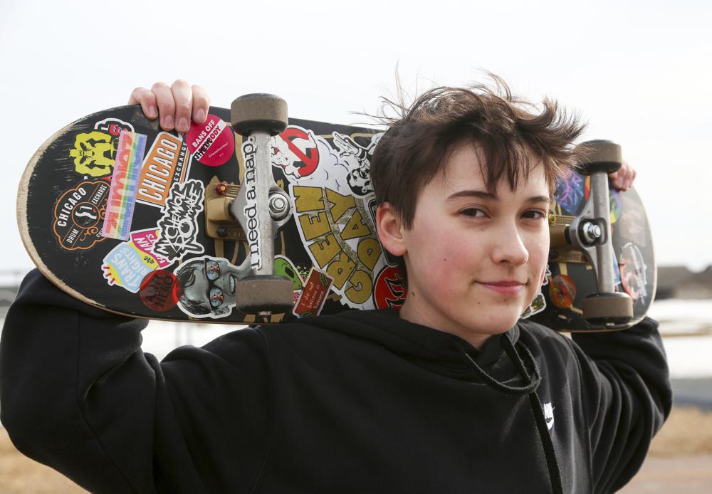 Asher Wilcox-Broekemeier, 13, poses for a portrait with his sticker-adorned skateboard, Monday, March 27, 2023, in Sioux Falls, S.D. Asher still struggles with moments of gender dysphoria. Friendships that were once strong fizzled after Asher came out as transgender. Parents have disinvited him from their houses out of fears he’s a “bad influence.” (AP Photo/Erin Woodiel)