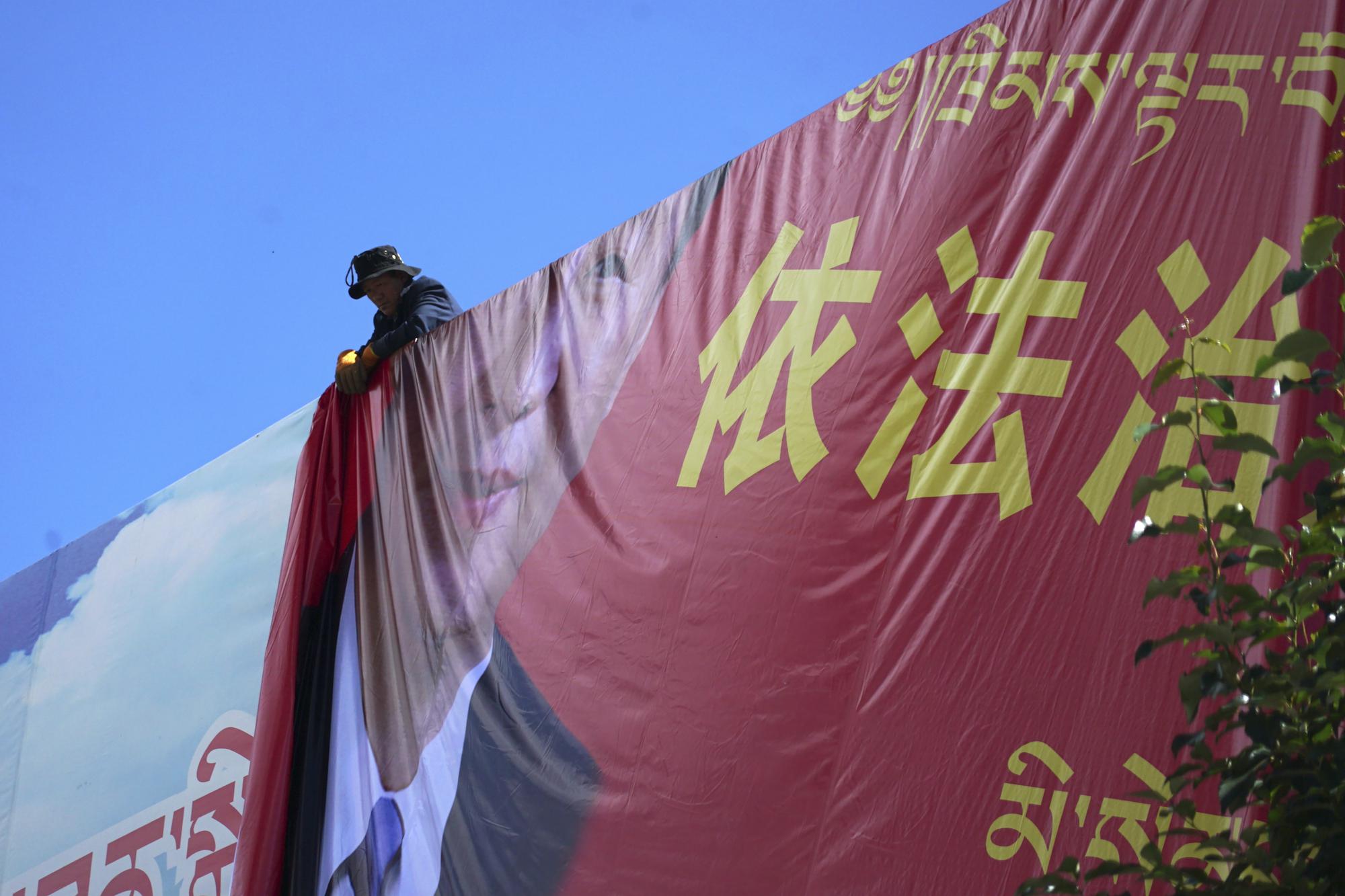 A man unfurls a banner reading "Govern the country in accordance with the law" and a picture of Chinese President Xi Jinping in the majority-Tibetan town of Litang, in southwestern China's Sichuan province on Sunday, Sept. 6, 2020. Ahead of the Beijing summer Olympics 14 years ago, Tibet was on fire. Deadly clashes between Tibetans and security forces in Lhasa made global headlines, and for weeks, monks and herders battled bullets and batons.  But today, Tibet has fallen silent, even as the Olympic games come to Beijing for a second time. (AP Photo/Dake Kang)