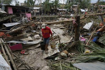 Un hombre carga cubos junto a casas dañadas por el tifón Rai en Talisay, en la provincia de Cebú, Filipinas, el viernes 17 de diciembre de 2021. (AP Foto/Jay Labra)