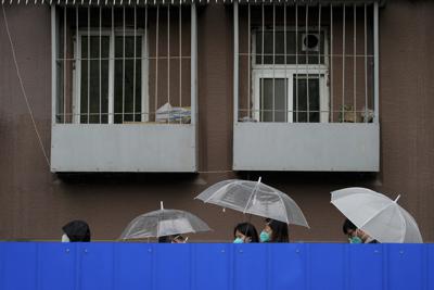 Residentes se resguardan bajo paraguas mientras esperan bajo la lluvia junto a una barrera para someterse a una prueba de detección del coronavirus, en un edificio confinado de Beijing, el 27 de abril de 2022. (AP Foto/Andy Wong)