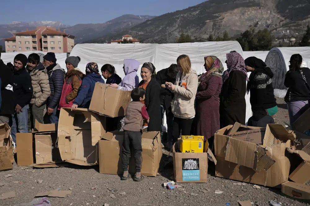 FILE - People who lost their houses in the devastating earthquake, lineup to receive aid supplies at a makeshift camp, in Iskenderun city, southern Turkey, Tuesday, Feb. 14, 2023. Hundreds of thousands of people are seeking shelter after the Feb. 6 earthquake in southern Turkey left homes unlivable. Many survivors have been unable to find tents or containers dispatched to the region by the government and aid agencies, Instead they have sought refuge in any structure that can protect them from the winter conditions, including greenhouses, rail carriages and factories.. (AP Photo/Hussein Malla)