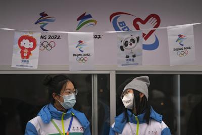 Voluntarias con mascarilla para evitar contagios de coronavirus charlan en un puesto de información para los Juegos Olímpicos de Invierno en la calle de Qianmen, un popular destino turístico en Beijing, el domingo 23 de enero de 2022. (AP Foto/Andy Wong)