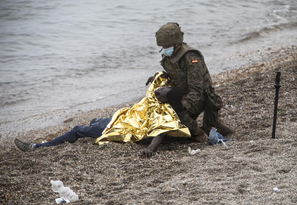 A man is assisted by a soldier of the Spanish Army near the border of Morocco and Spain, at the Spanish enclave of Ceuta, on Tuesday, May 18, 2021. About 8,000 people have streamed into the Spanish city of Ceuta from Morocco in the past two days in an unprecedented influx of migrants, most of them swimming across the border to reach the Spanish enclave in North Africa.(AP Photo/Javier Fergo)