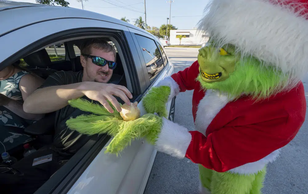 In this photo provided by the Florida Keys News Bureau, a Maryland motorist, left, accepts an onion instead of a traffic citation from Monroe County Sheriff's Office Colonel Lou Caputo, right, costumed as the Grinch, Tuesday, Dec. 13, 2022, in Marathon, Fla. For drivers slightly speeding through a school zone on the Florida Keys Overseas Highway Tuesday, Caputo offered them the choice between an onion or a traffic citation. It's a holiday tradition in the Keys that Caputo began 20 years ago to educate drivers that Keys schools remain in session through Dec. 16. (Andy Newman/Florida Keys News Bureau via AP)