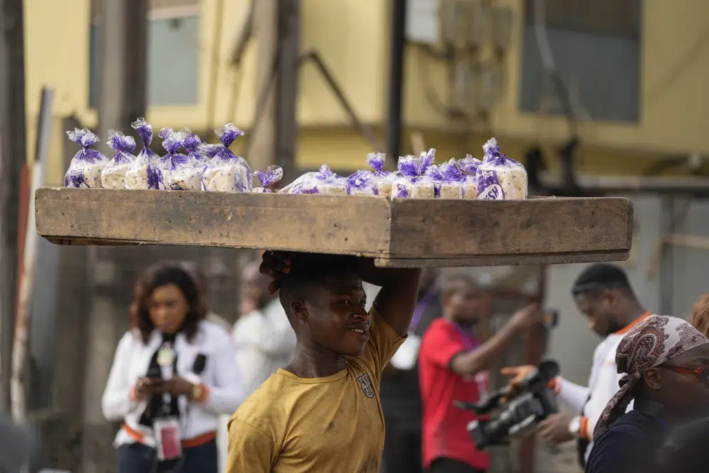 A street vendor carries packets of bread to sell next to a polling station during the presidential elections in Lagos, Nigeria, Saturday, Feb. 25, 2023. Voters in Africa's most populous nation are heading to the polls Saturday to choose a new president, following the second and final term of incumbent Muhammadu Buhari. (AP Photo/Ben Curtis)