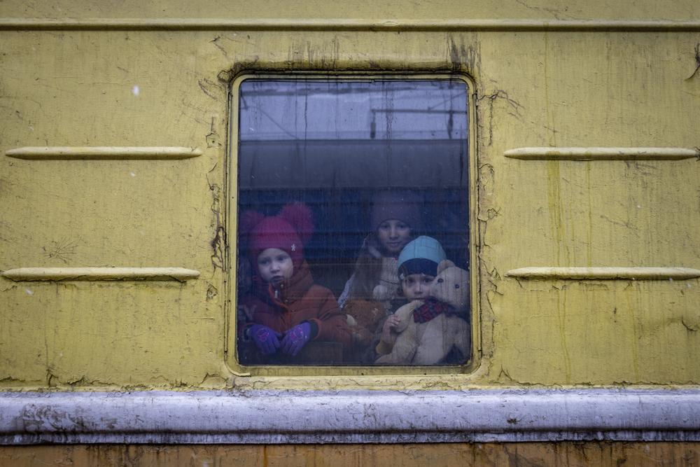Children Vlada, left, Katrin and Danilo look out from a window of an unheated train carriage of an emergency evacuation train which is travelling from Kharkov to Lviv, as it stopped in the Kyiv railway station in Kyiv, Ukraine, Thursday, March 3, 2022. (AP Photo/Andriy Dubchak)