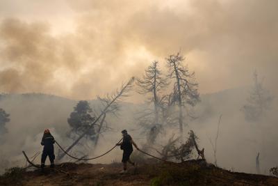 ARCHIVO - En imagen de archivo del lunes 9 de agosto de 2021, un bombero combate las llamas al tiempo que un civil sostiene una manguera durante un incendio forestal en la aldea de Ellinika, en la isla de Evia, aproximadamente a 176 kilómetros (110 millas) al norte de Atenas. (AP Foto/Petros Karadjias, archivo)