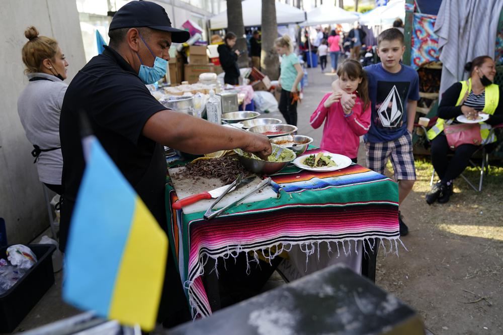El voluntario mexicano Félix Lara prepara tacos para refugiados ucranianos en un campamento improvisado cerca de la frontera, el lunes 4 de abril de 2022 en Tijuana, México.  Voluntarios de México y Estados Unidos están ayudando a cientos de refugiados diariamente, donde esperan de dos a cuatro días para que los funcionarios estadounidenses los admitan en libertad condicional humanitaria.  (Foto AP/Gregory Bull)