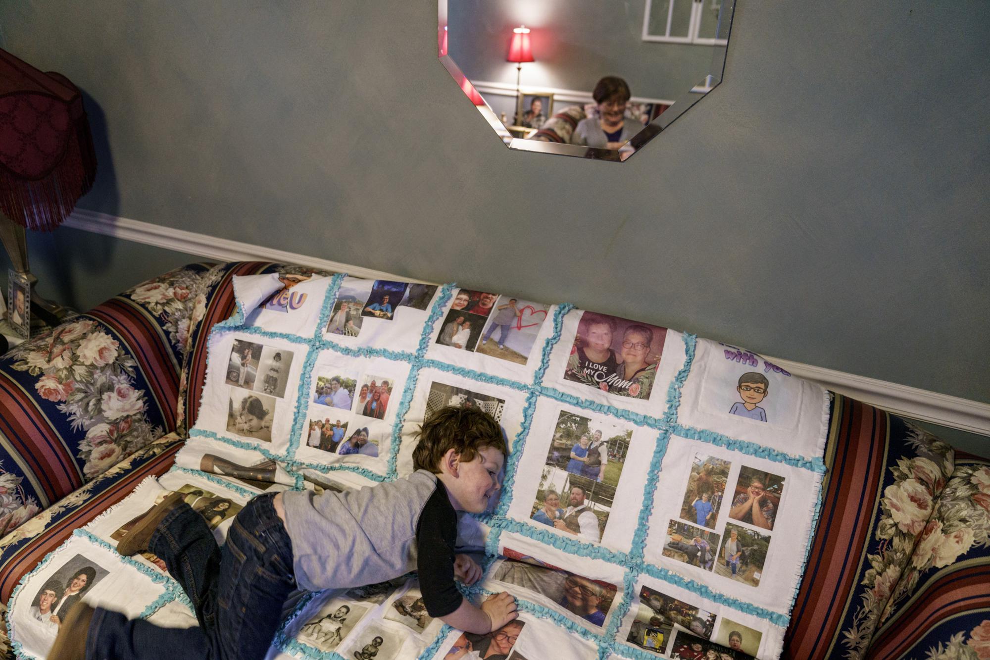 Killian McClung, 3, plays on a memorial quilt for his grandmother, Jennifer McClung, as her mother, Stella Olive, reflected in mirror, looks on at her home in Muscle Shoals, Ala., Monday, March 7, 2022. One of McClung's greatest joys was caring for Killian, whom she called her "grandblessing." When he asked where she'd gone, family members made him a book showing McClung dressed like an astronaut, smiling back from space. On Dec. 14, 2020, McClung, a nurse, died of COVID-19, just hours before the nation's vaccination campaign began. (AP Photo/David Goldman)