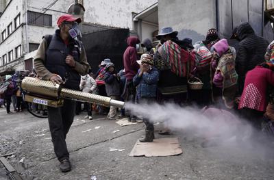 Un trabajador rocía desinfectante alrededor de las personas que viajaron desde las provincias a la iglesia Monte de Oración para comprar alimentos y ropa durante la campaña anual del Buen Samaritano de la iglesia en La Paz, Bolivia, el martes 28 de diciembre de 2021. Debido a la pandemia de COVID-19, la iglesia está distribuyendo la mercadería al aire libre. (AP Foto/Freddy Barragan)