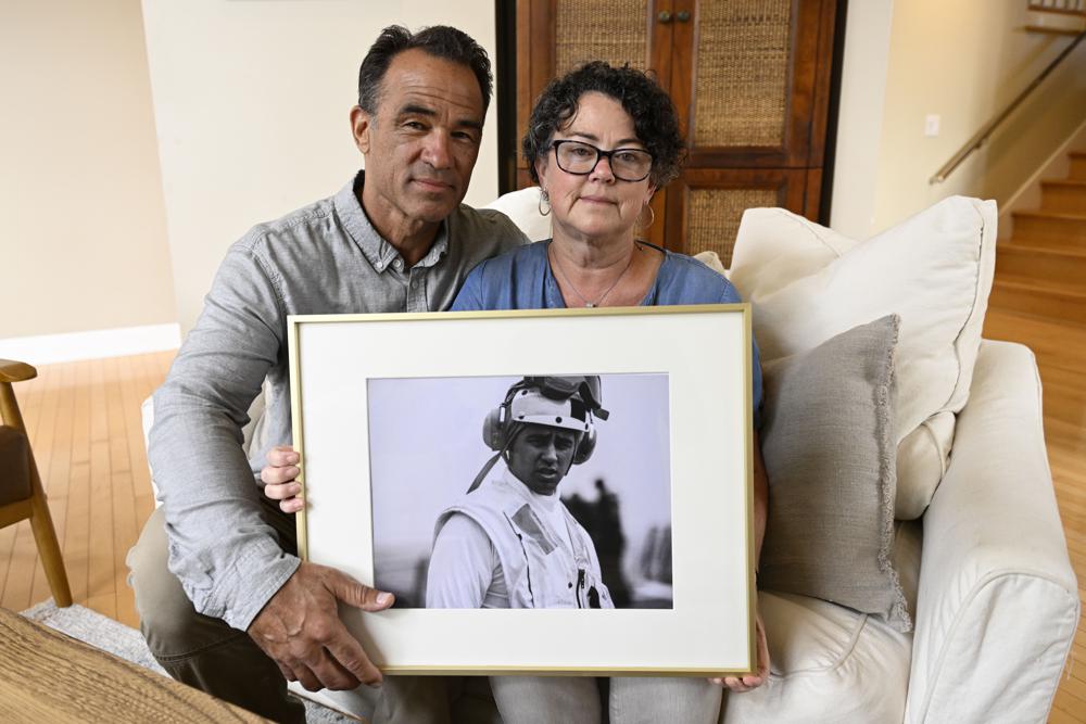 Derek and Suzi Alkonis pose with a photo of their son Lt. Ridge Alkonis on Wednesday, June 1, 2022, in Dana Point, Calif. Their son, a U.S. Navy lieutenant in Japan, faces a potential three-year prison sentence for a car crash that killed two people last year. The family of Alkonis says he suffered from acute mountain-sickness and passed out unconscious behind the wheel. Japanese prosecutors and a judge say he was feeling drowsy and should have pulled over. (AP Photo/Denis Poroy)