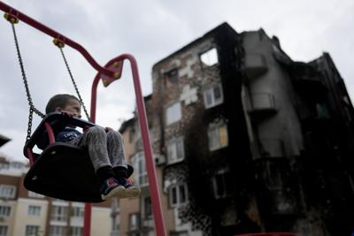 Yarik juega en un patio de recreo frente a un edificio destruido durante los ataques en las afueras de Irpin Kiev, Ucrania, el lunes 30 de mayo de 2022. (AP Foto/Natacha Pisarenko)