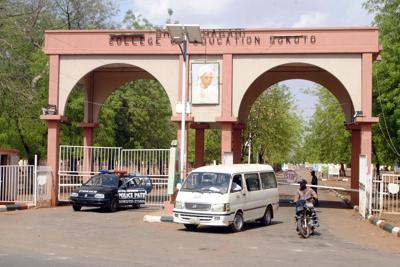 Un hombre conduce un mototaxi el viernes 13 de mayo de 2022 frente a los vehículos de la policía en la entrada del Colegio de Educación Shehu Shagari en Sokoto, Nigeria. (AP Foto/Olu Akinrele)