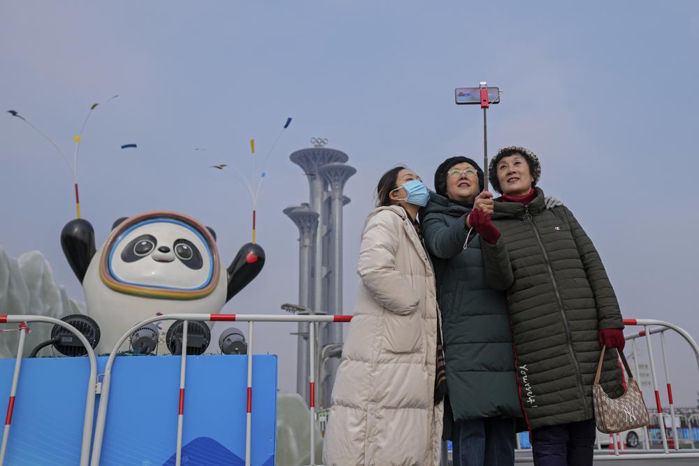 Una mujer que usa una máscara facial para ayudar a protegerse del coronavirus se toma una selfie con su acompañante contra una mascota de los Juegos Olímpicos de Invierno de Beijing y la Torre Olímpica en Beijing, el miércoles 19 de enero de 2022. China ha bloqueado partes del distrito Haidian de Beijing luego de la detección de tres casos, apenas unas semanas antes de que la capital sea sede de los Juegos Olímpicos de Invierno.  (Foto AP/Andy Wong)