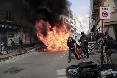 Manifestantes caminan cargando una manta junto a basura y escombros a los que se les prendió fuego durante una marcha por el Día Internacional de los Trabajadores, el domingo 1 de mayo de 2022, en París, Francia. (AP Foto/Lewis Joly)