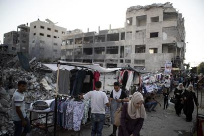 ARCHIVO - En esta imagen del domingo 18 de julio de 2021, vendedores callejeros palestinos muestran ropa a la venta junto a escombros de edificios derruidos por ataques aéreos israelíes durante la guerra de 11 días entre Hamas, que gobierna Gaza, e Israel, en Ciudad de Gaza. (AP Foto/Khalil Hamra, Archivo)