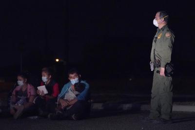 En esta imagen del 24 de marzo de 2021, un inmigrante, al centro, carga a un niño mientras mira a un agente de la Oficina de Aduanas y Protección Fronteriza en una zona de detención después de cruzar la frontera entre México y Estados Unidos, en Roma, Texas. (AP Foto/Julio Cortez)