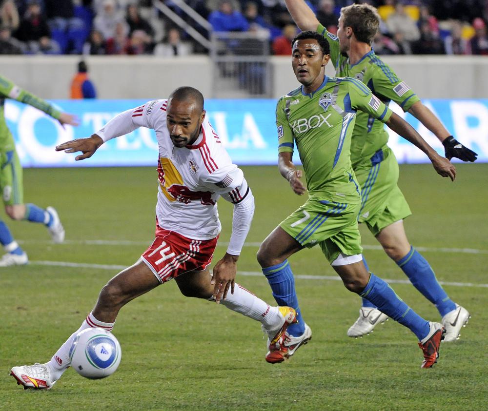 FILE -New York Red Bulls' Thierry Henry (14) dribbles the ball as he is trailed by Seattle Sounders' James Riley and Jeff Parke, right, during the first half of an MLS soccer game Saturday, March 19, 2011 in Harrison, N.J. Thierry Henry was long removed from his days as a star for Arsenal when he joined the New York Red Bulls in 2010. (AP Photo/Bill Kostroun, File)