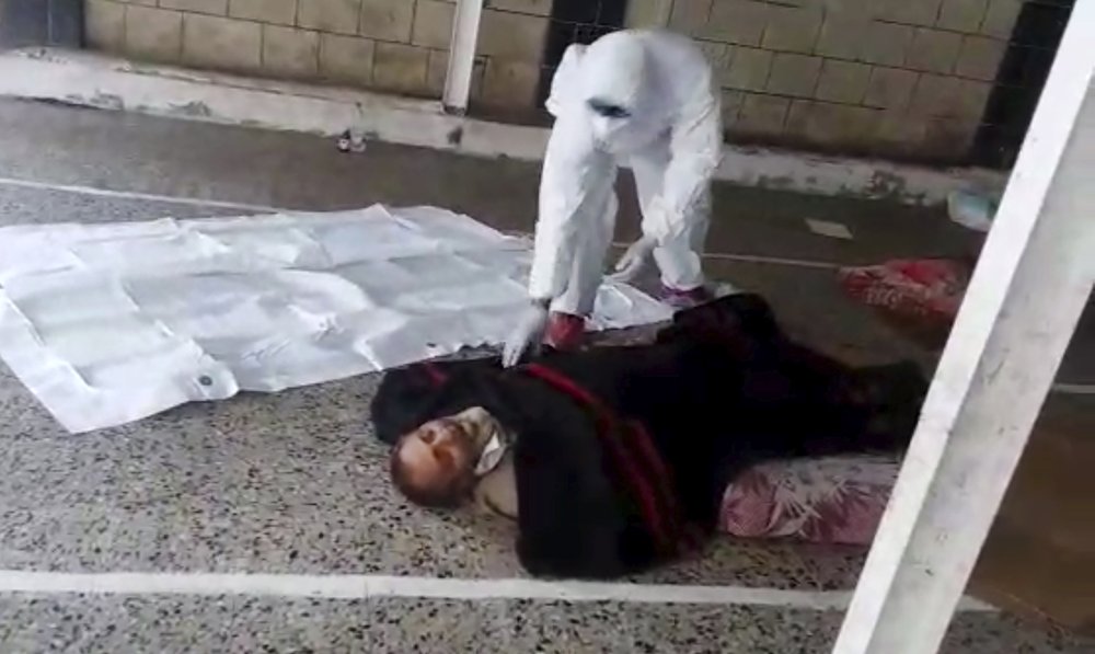This May 2020 frame grab from video provided by a Yemeni Community activist, shows an activist wearing protective gear collecting the body of a COVID-19 victim, after medics declined to take the body, in the Houthi-controlled city of Ibb, Yemen. An investigation by The Associated Press found that the coronavirus is taking a deadly toll on the war weary population of Yemen. The situation is exacerbated in the Houthi-controlled north where the rebels have suppressed information about the virus, severely punished those who speak out, enforced little mitigation measures, and promoted conspiracies and claims by the Houthi minister of health that scientists are working on developing a cure for covid-19 to present to the world. (Courtesy of a Yemeni Community Activist via AP)