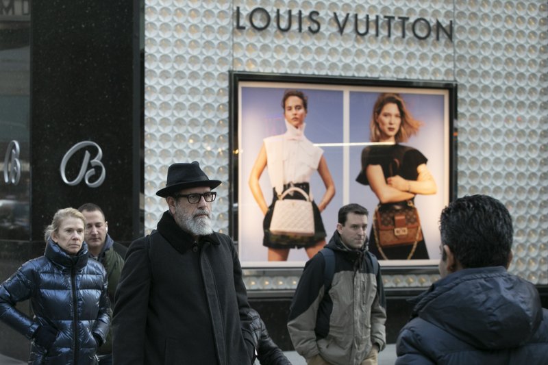 People pass a store window for Louis Vuitton, Monday, Nov. 25, 2019 in New York. French luxury group LVMH has agreed to buy iconic New York jeweler Tiffany & Co. for $16.2 billion, adding a famed star to its portfolio that already boasts Louis Vuitton, Christian Dior and Bulgari. (AP Photo/Mark Lennihan)