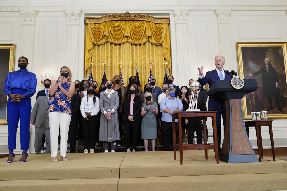 President Joe Biden, right, speaks as he welcomes the Seattle Storm to the East Room of the White House in Washington, Monday, Aug. 23, 2021, for their 2020 WNBA Championship. Going him on stage is Crystal Langhorne, former Seattle Storm player and Director of Community Engagement, Force4Change, left, and Ginny Gilder, Seattle Storm owner, second from left. (AP Photo/Susan Walsh)