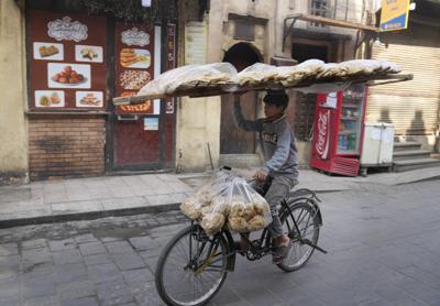A vendor balances a tray of Egyptian traditional "Baladi" flatbread as he cycles in Old Cairo district, Egypt, Tuesday, March 22, 2022. Experts say they are worried that food security concerns in the Middle East resulting from the war in Ukraine may fuel growing social unrest in countries already on the verge of meltdown. (AP Photo/Amr Nabil)