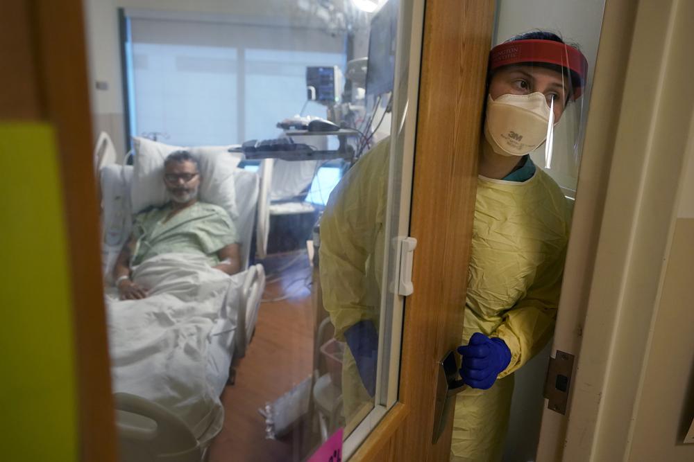 Registered nurse Rachel Chamberlin, of Cornish, N.H., right, steps out of an isolation room where where Fred Rutherford, of Claremont, N.H., left, recovers from COVID-19 at Dartmouth-Hitchcock Medical Center, in Lebanon, N.H., Monday, Jan. 3, 2022. Hospitals like this medical center, the largest in New Hampshire, are overflowing with severely ill, unvaccinated COVID-19 patients from northern New England. If he returns home, Rutherford said, he promises to get vaccinated and tell others to do so, too. (AP Photo/Steven Senne)