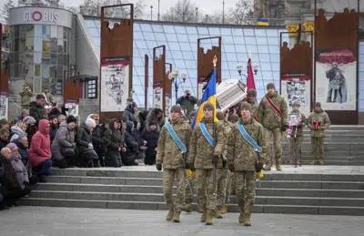 Unas personas se arrodillan mientras militares ucranianos cargan el ataúd de su compañero Oleh Yurchenko, quien murió en un enfrentamiento contra fuerzas rusas en la región de Donetsk, durante una ceremonia en Kiev, el domingo 8 de enero de 2023. (AP Foto/Efrem Lukatsky)