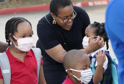 Leandra Walker, al centro, ayuda a su hija Mila Walker, de 5 años, a ponerse su mascarilla antes de que entre a la escuela con sus hermanos Olivia, de 7 años, izquierda, y su mellizo Max para el primer día de clases, el martes 17 de agosto de 2021, en Richardson, Texas. (AP Foto/LM Otero)