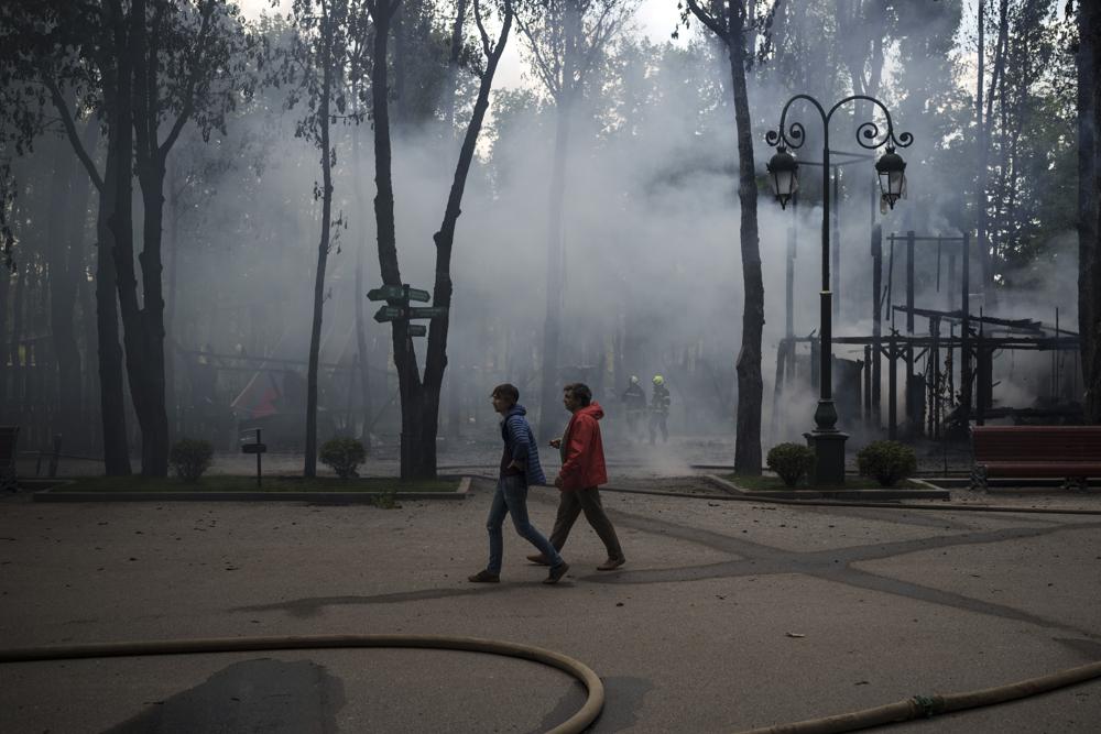 Gente atravesando un parque mientras bomberos apagan un incendio tras un bombardeo ruso en Járkiv, Ucrania, martes 3 de mayo de 2022. (AP Foto/Felipe Dana)