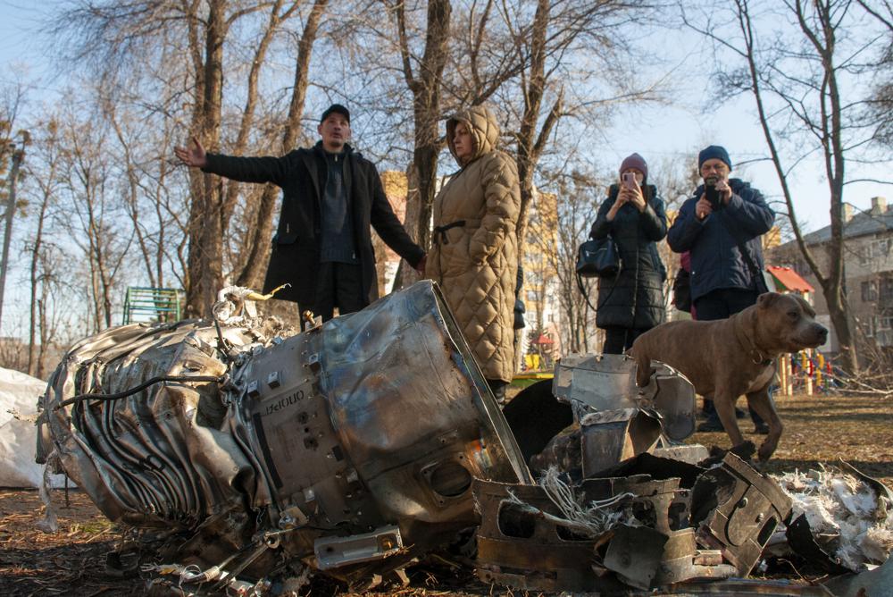 People stand next to fragments of military equipment on the street in the aftermath of an apparent Russian strike in Kharkiv in Kharkiv, Ukraine, Thursday, Feb. 24, 2022. Russian troops have launched their anticipated attack on Ukraine. Big explosions were heard before dawn in Kyiv, Kharkiv and Odesa as world leaders decried the start of an Russian invasion that could cause massive casualties and topple Ukraine's democratically elected government. (AP Photo/Andrew Marienko )