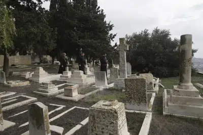 Hosam Naoum, un obispo anglicano palestino, camina junto a otros religiosos por el lugar donde unos vándalos atacaron más de 30 tumbas en un histórico cementerio protstante en el Monte Zión, en Jerusalén, el 4 de enero de 2023. (AP Foto/ Mahmoud Illean)